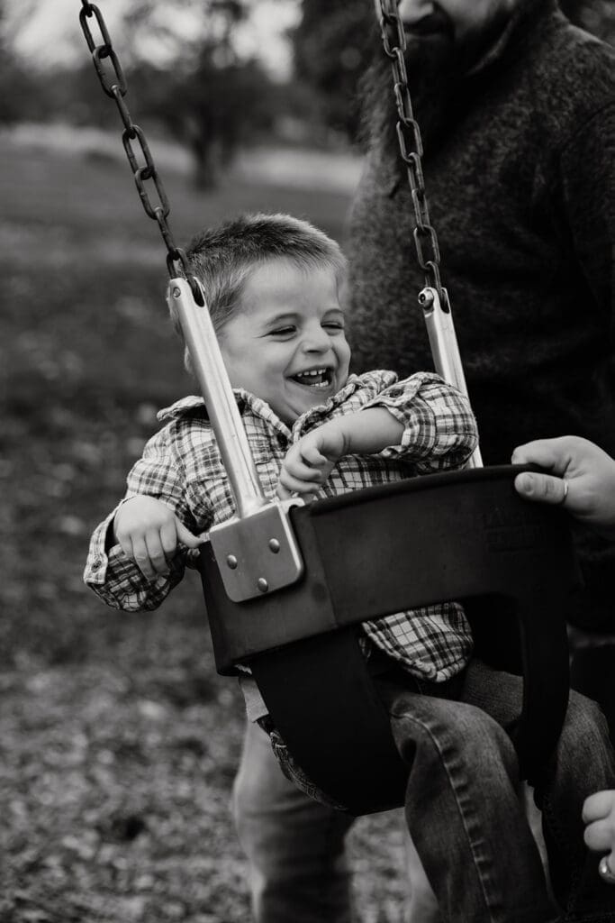Documentary style family photographer capturing real connection in an Eastern Iowa playground with mom pushing toddler in swing.