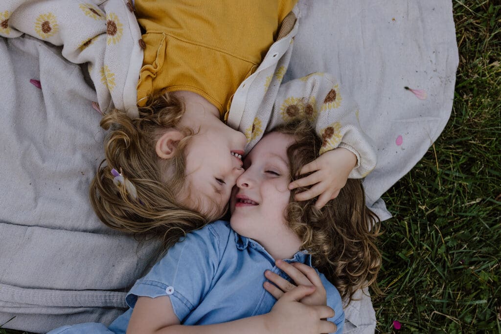 Candid photo of two young siblings laying down touching noses during a Cedar Rapids, Iowa relaxed backyard family picture session.