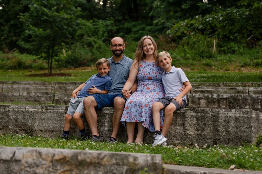 Family of 4 sitting smiling at the camera during a family photo session at Indian Creek Nature Center in Cedar Rapids, Iowa.