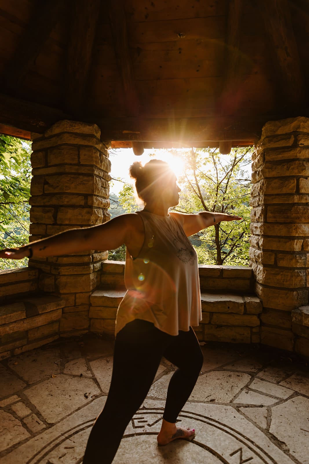 Yoga instructor holding a yoga pose at a Cedar Rapids, Iowa park during a business branding photo session in the center of stone structure with sun flare from sunset peeking through.