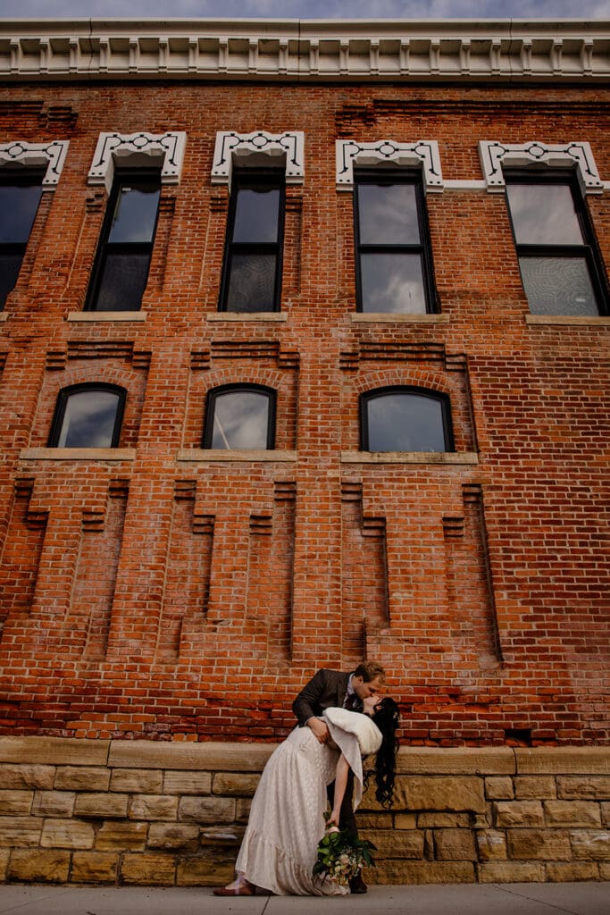 Romantic urban elopement photo session in downtown Marion, Iowa, groom dipping bride for a kiss in front of historic brick building.
