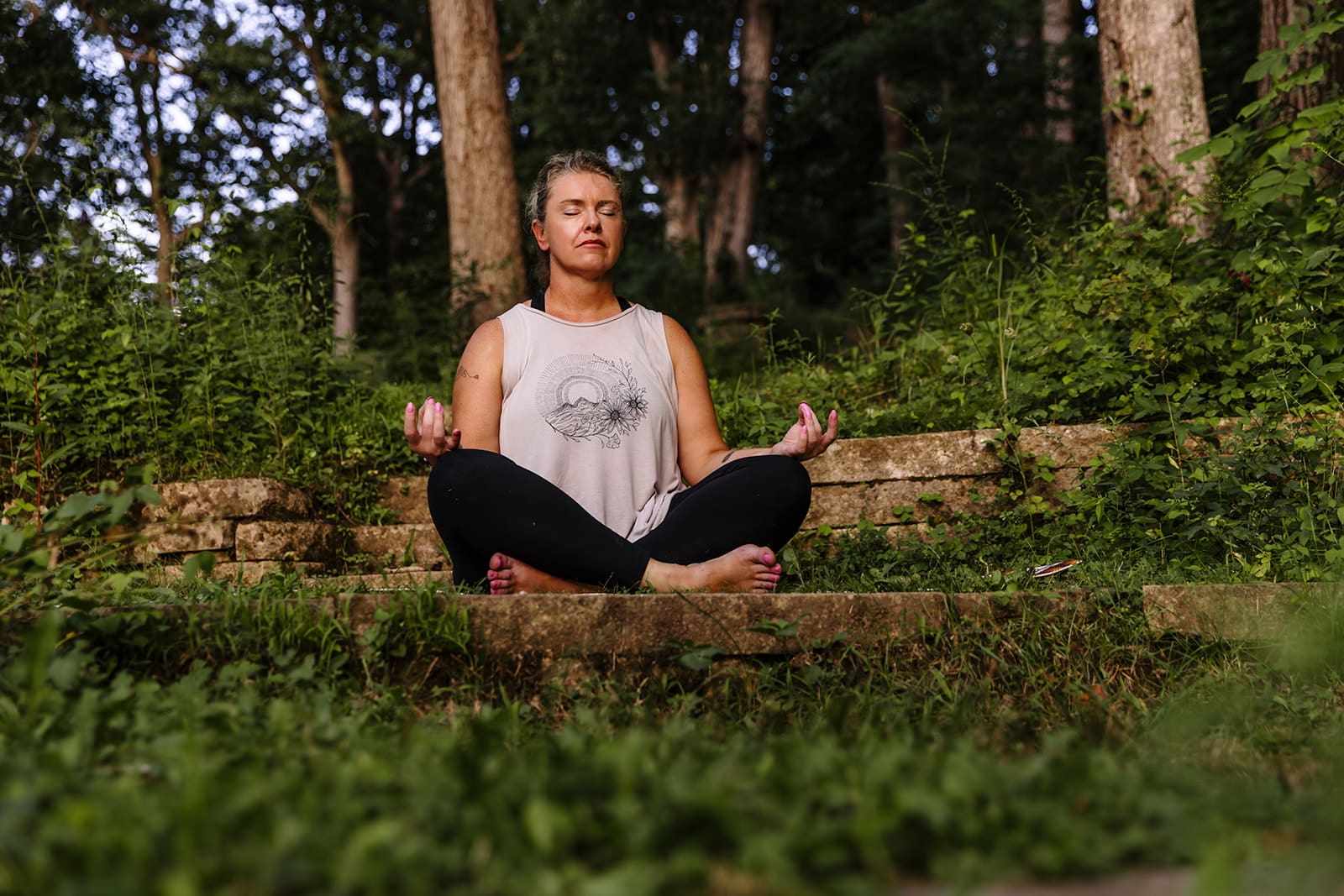 Yoga instructor sitting outdoors in meditation pose during a business branding photo session in Eastern Iowa park.